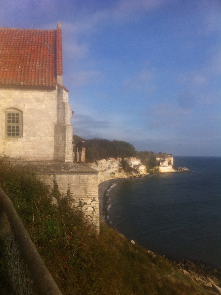 Højerup kirke, med krittklippen i bakgrunnen. Askelaget fra k-t grensen ligger omtrent halvveis opp på klippeveggen, der det er dannet et overheng på grunn av den hardere bergarten ovenfor.